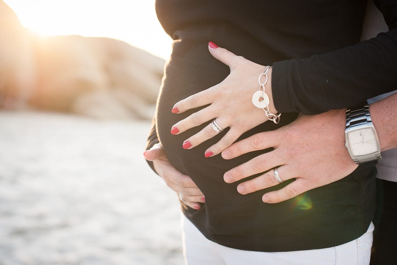 close up on pregnant woman holding her belly on the beach