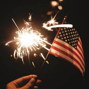 Person holding sparkler firework and a small American flag