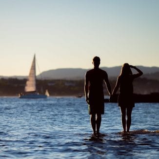 Couple at ocean with sailboat in background
