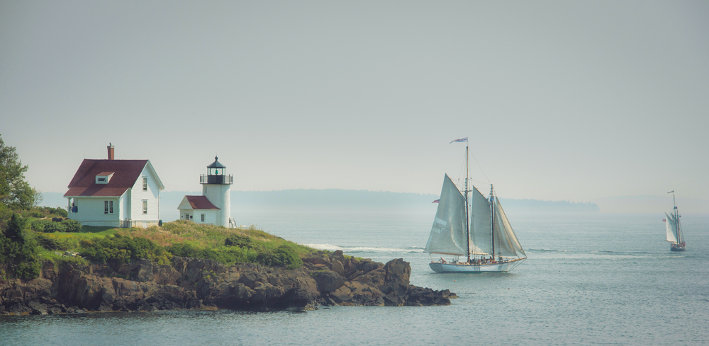 sailboats passing a lighthouse
